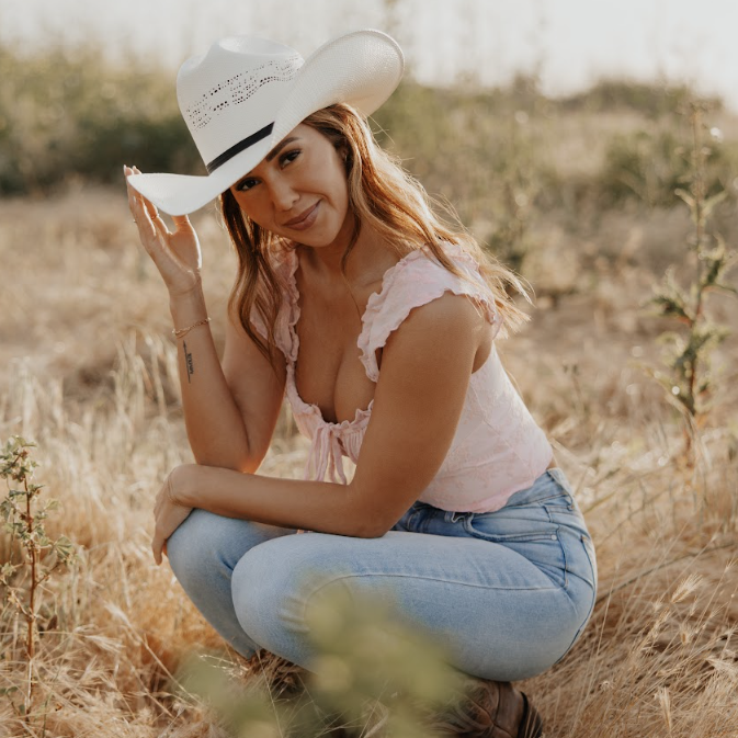 Image of Woman wearing a white cowboy hat and pink top in a field