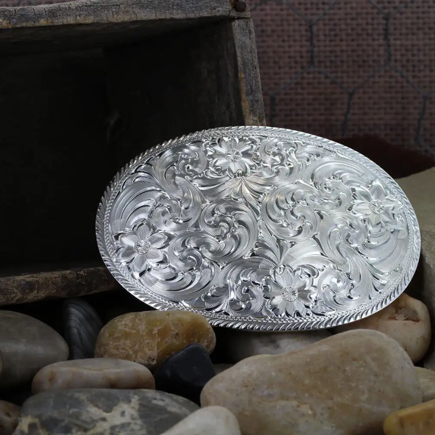 Image of Decorative silver belt buckle on a bed of stones with a wooden box in the background