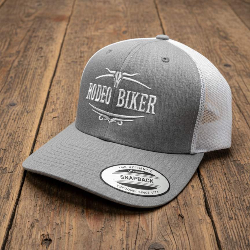 Image of Gray and white cap with 'Rodeo Biker' text on a wooden surface