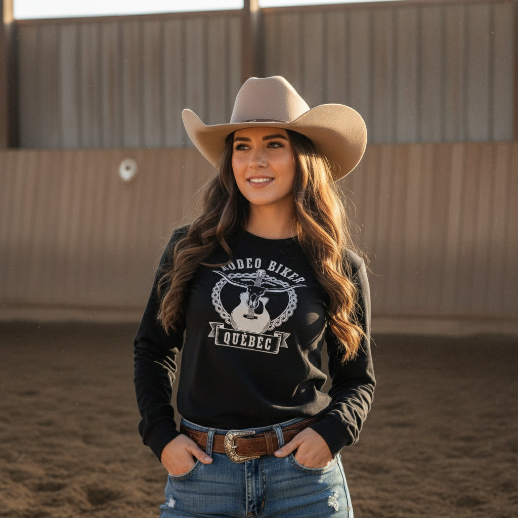Image of Woman wearing a black sweatshirt with a graphic design, standing in front of a wooden fence with a field and sky background.