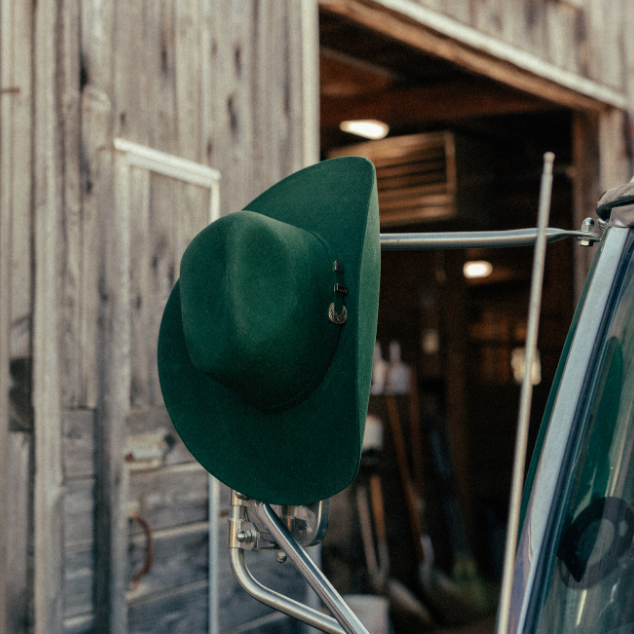 Image of Green hat on a car mirror with a rustic wooden building in the background