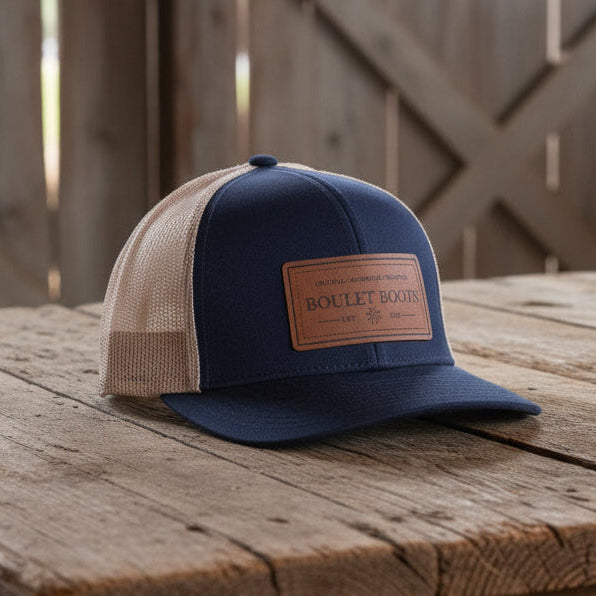 Image of Navy and beige cap with a brown leather patch on a white background