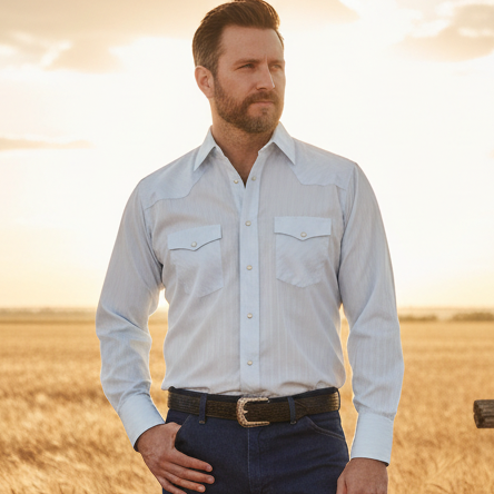 Image of A man wearing a light blue long-sleeve western shirt, dark blue jeans, a black belt, and a black cowboy hat, photographed against a plain light gray studio background.