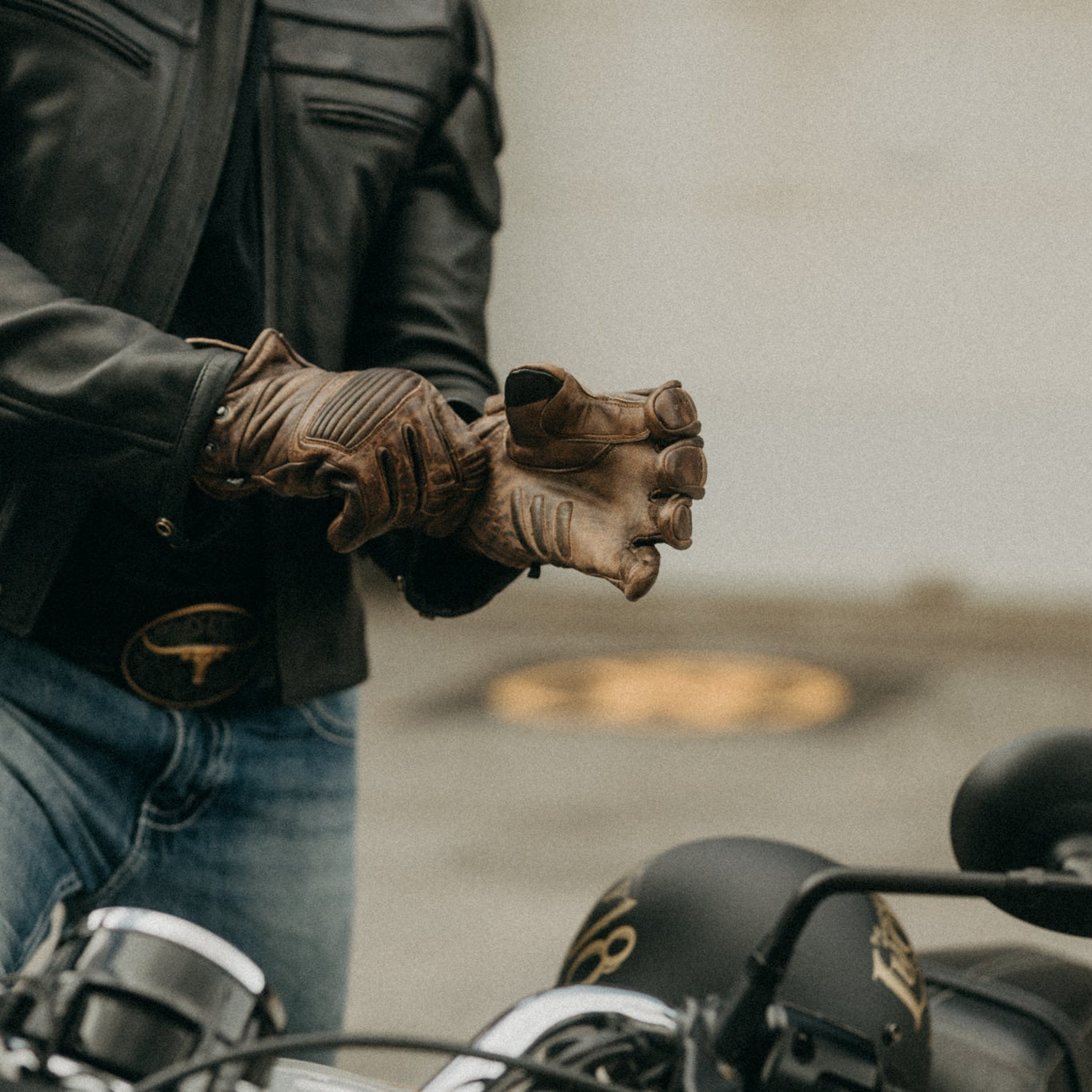 Image of Person wearing a leather jacket and gloves on a motorcycle with a blurred background