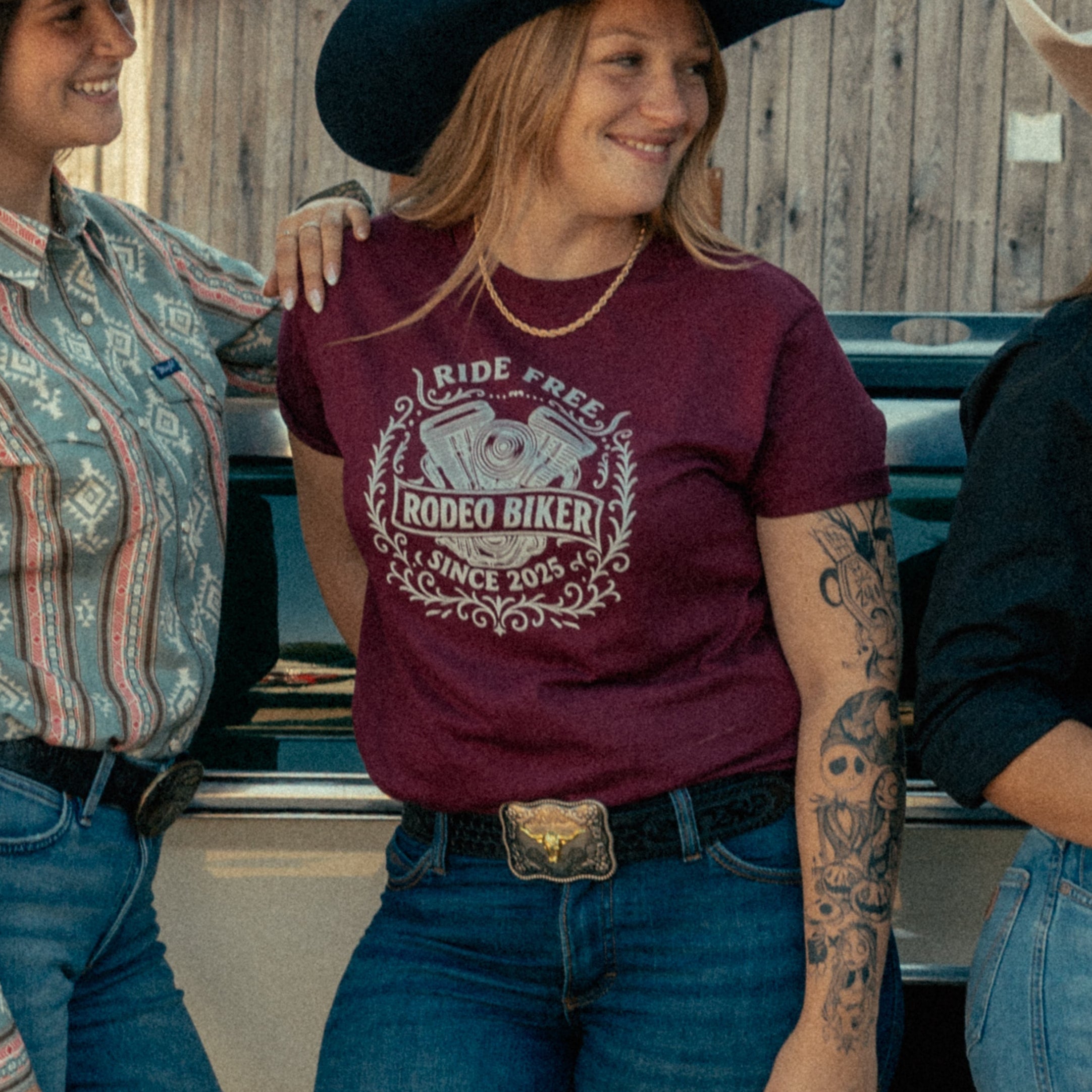 Image of Three women posing together in front of a rustic wooden building and a vintage pickup truck, wearing western-style clothing including cowboy hats, jeans, and boots.