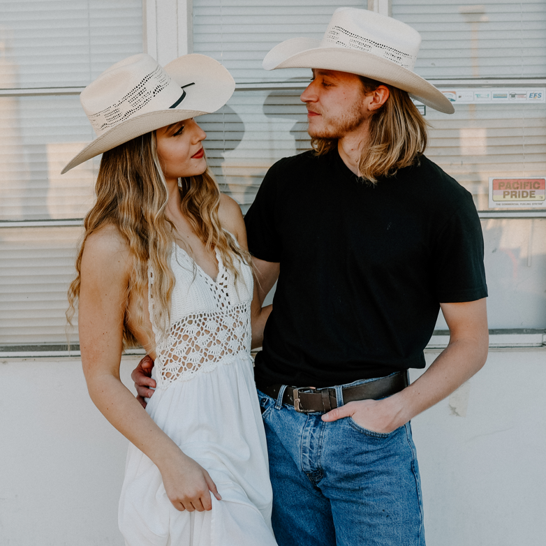 Image of Man and woman wearing cowboy hats standing close to each other outdoors.