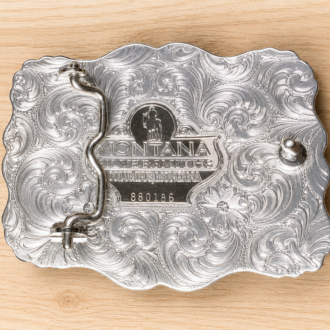 Image of Silver belt buckle with intricate designs on a wooden surface