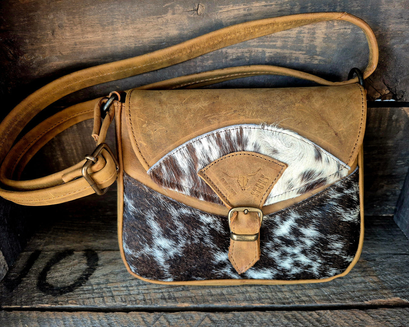 Image of Brown leather and cowhide patterned bag on a wooden surface