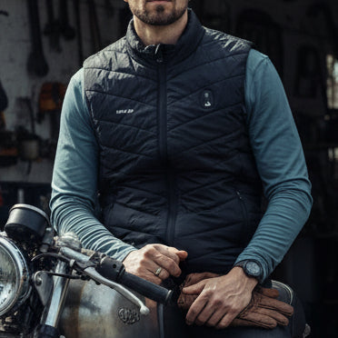 Image of Man wearing a black quilted vest over a teal long-sleeve shirt on a white background